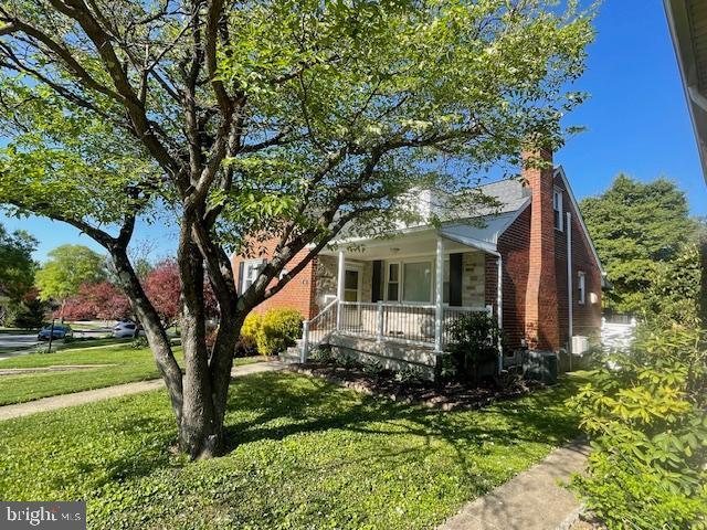bungalow-style home with a front lawn, covered porch, and a chimney
