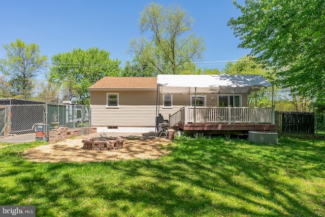 rear view of house featuring a fire pit, a wooden deck, a yard, and fence