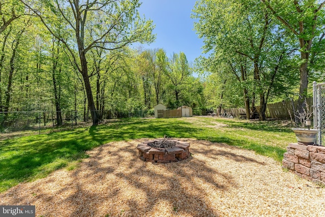 view of yard featuring a storage unit, a fenced backyard, an outdoor fire pit, and an outdoor structure