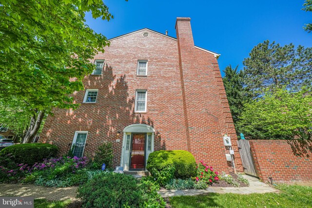 tudor house featuring brick siding, fence, a chimney, and a gate
