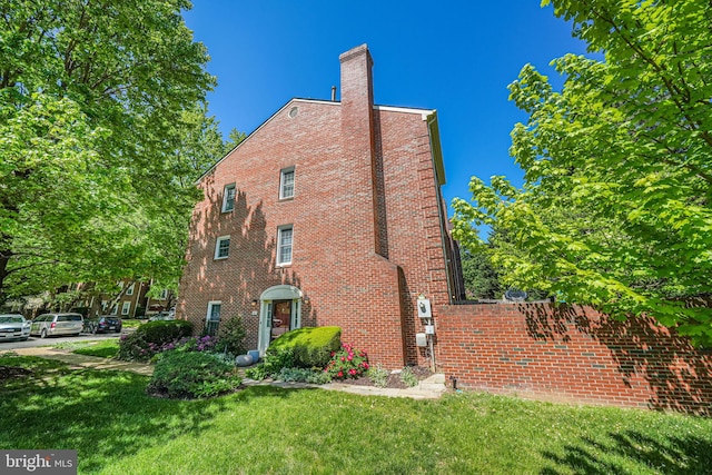 view of side of home featuring a chimney, a yard, and brick siding