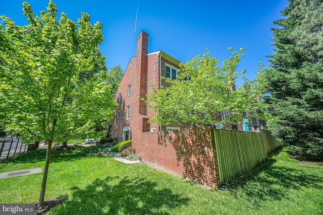 view of home's exterior featuring fence, a chimney, a lawn, and brick siding