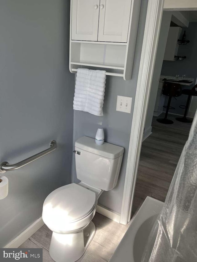 bathroom featuring toilet, baseboards, a washtub, and wood finished floors