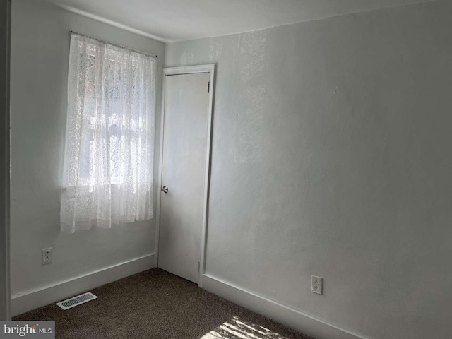 spare room with plenty of natural light, dark colored carpet, and visible vents