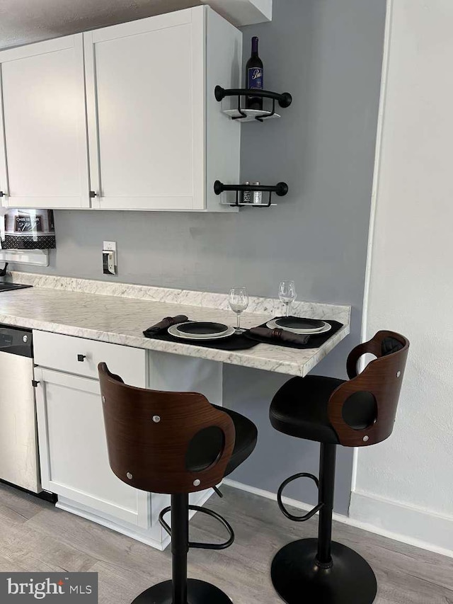 kitchen with white cabinetry, light wood-style floors, baseboards, and dishwasher