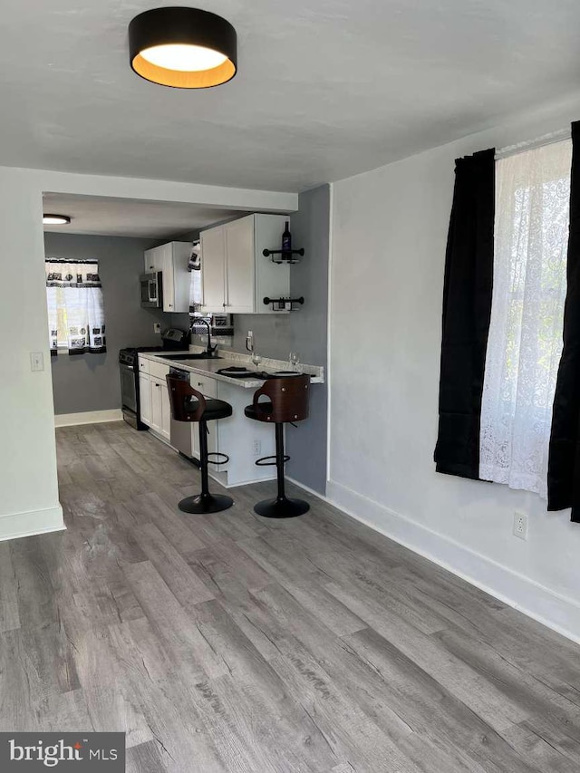 kitchen with appliances with stainless steel finishes, open shelves, wood finished floors, a breakfast bar, and white cabinetry