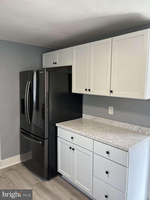 kitchen with baseboards, white cabinets, black fridge, and light wood-style flooring