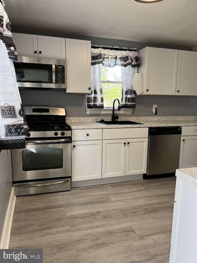 kitchen featuring a sink, appliances with stainless steel finishes, white cabinets, and light countertops