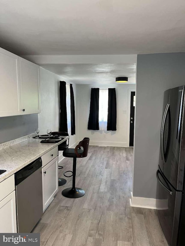kitchen with light wood-style floors, dishwasher, freestanding refrigerator, white cabinetry, and baseboards