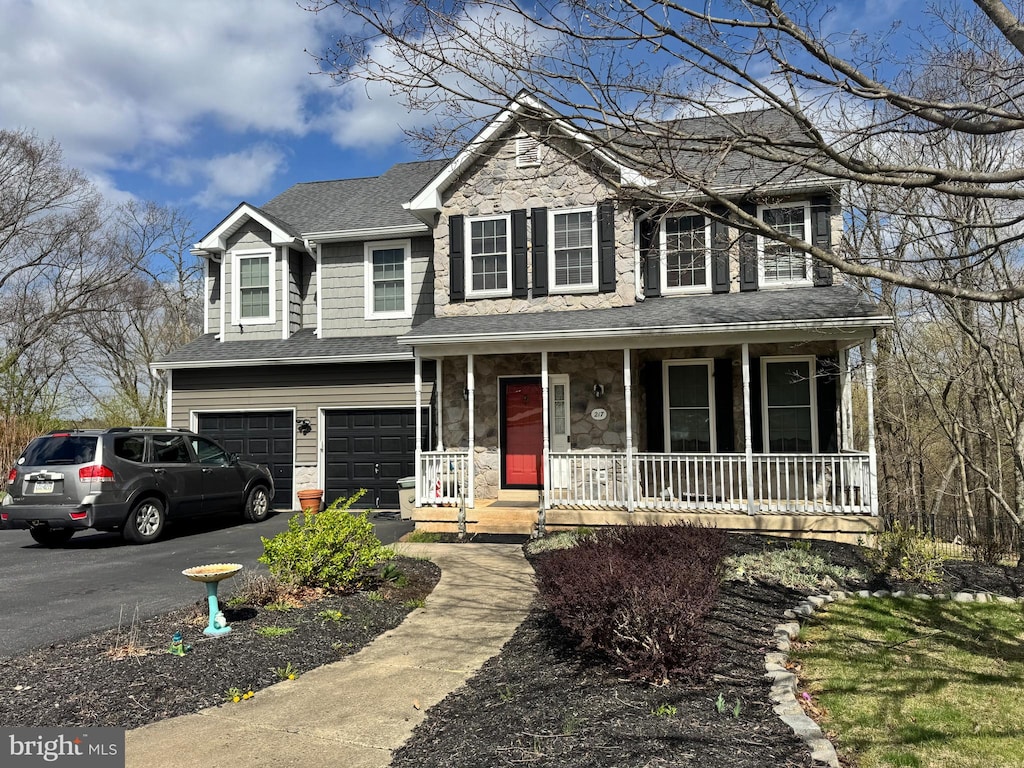 view of front of house featuring roof with shingles, stone siding, a garage, a porch, and driveway