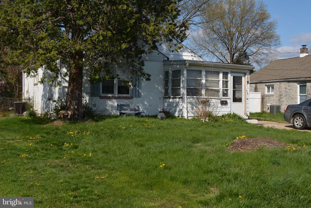 view of front of house with a sunroom, a front lawn, and central air condition unit
