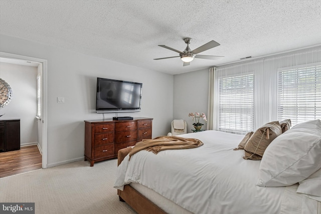 bedroom featuring light colored carpet, a textured ceiling, baseboards, and visible vents
