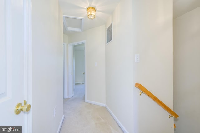 hallway with attic access, visible vents, light colored carpet, baseboards, and an upstairs landing