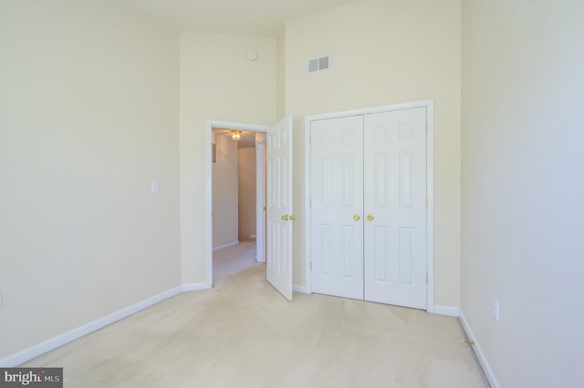 unfurnished bedroom featuring visible vents, a closet, baseboards, high vaulted ceiling, and carpet