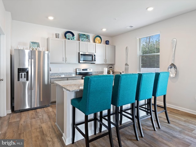 kitchen featuring a breakfast bar area, appliances with stainless steel finishes, a center island with sink, wood finished floors, and recessed lighting