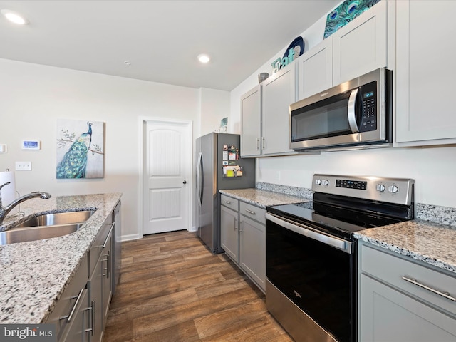 kitchen featuring light stone countertops, dark wood-style floors, gray cabinets, a sink, and appliances with stainless steel finishes