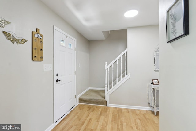 foyer featuring baseboards, stairs, and light wood finished floors