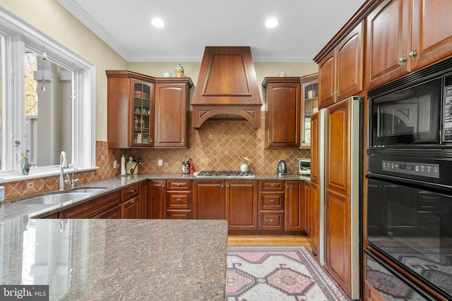kitchen with glass insert cabinets, a sink, premium range hood, black appliances, and stone counters