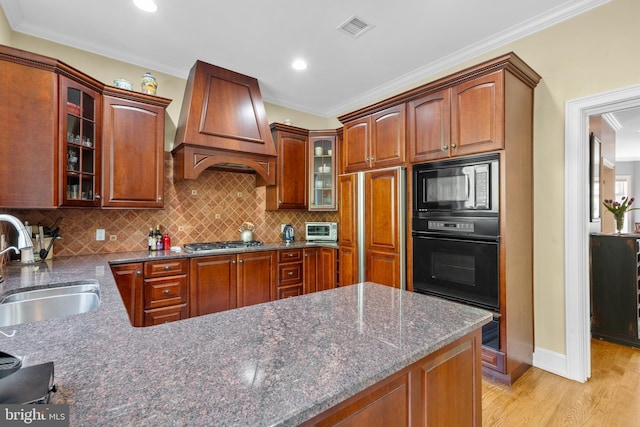 kitchen featuring visible vents, tasteful backsplash, a sink, built in appliances, and custom range hood