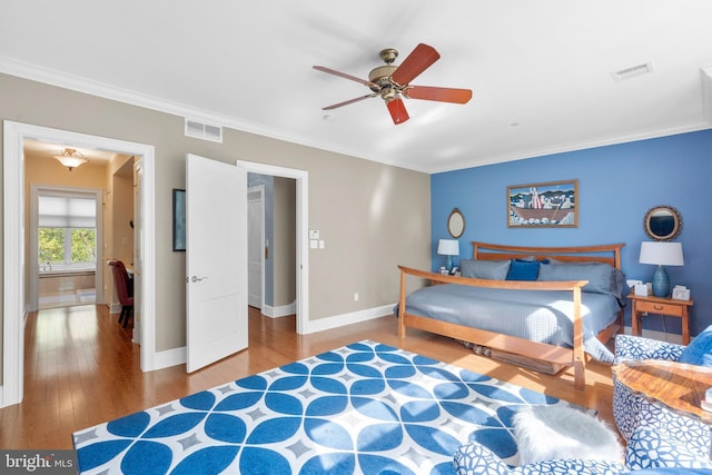 bedroom with baseboards, ornamental molding, wood finished floors, and visible vents
