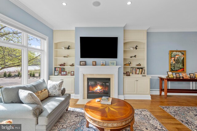 living area with a glass covered fireplace, ornamental molding, built in shelves, and light wood finished floors