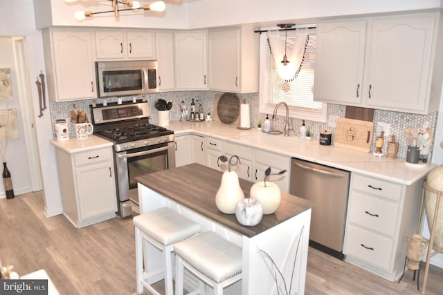 kitchen featuring a sink, light wood finished floors, appliances with stainless steel finishes, backsplash, and a notable chandelier