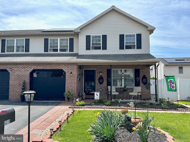 view of front of house featuring brick siding, a garage, a porch, roof mounted solar panels, and driveway