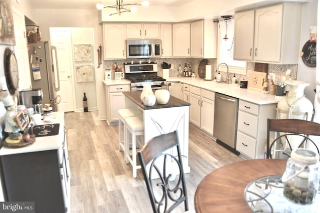 kitchen with appliances with stainless steel finishes, a sink, light countertops, light wood-style flooring, and tasteful backsplash
