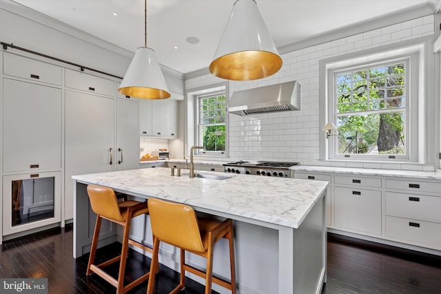 kitchen with dark wood-type flooring, wall chimney exhaust hood, white cabinets, tasteful backsplash, and a sink