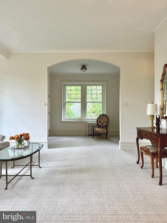 sitting room with light colored carpet, crown molding, arched walkways, baseboards, and radiator