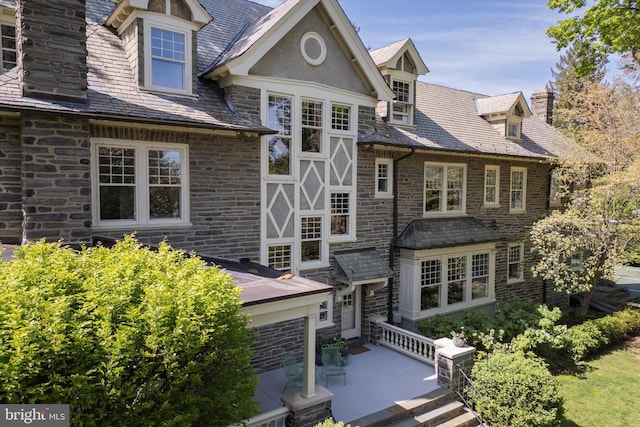 view of front of house with a high end roof, a chimney, and stone siding