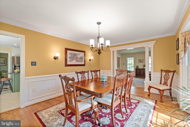dining space featuring crown molding, a wainscoted wall, decorative columns, and light wood finished floors