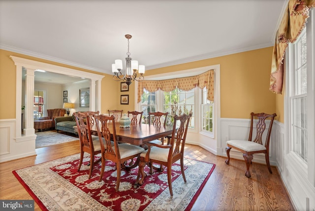 dining space featuring crown molding, wainscoting, light wood finished floors, and an inviting chandelier