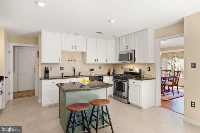 kitchen with decorative backsplash, dark countertops, white cabinetry, a sink, and appliances with stainless steel finishes