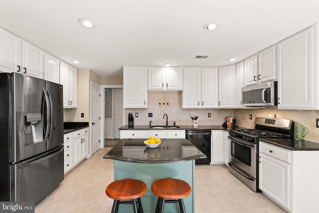 kitchen featuring a kitchen island, a breakfast bar, white cabinets, a sink, and appliances with stainless steel finishes