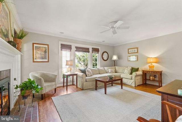 living area with crown molding, ceiling fan, a tiled fireplace, and wood finished floors