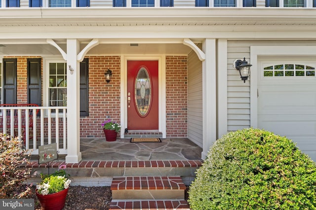 doorway to property with a garage, a porch, and brick siding