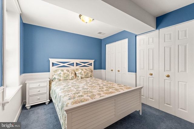 bedroom with dark colored carpet, wainscoting, multiple closets, and visible vents