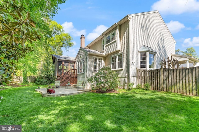 rear view of property with fence, a sunroom, a chimney, a patio, and a yard