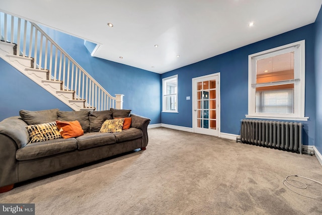 living room featuring carpet floors, radiator, baseboards, and stairway