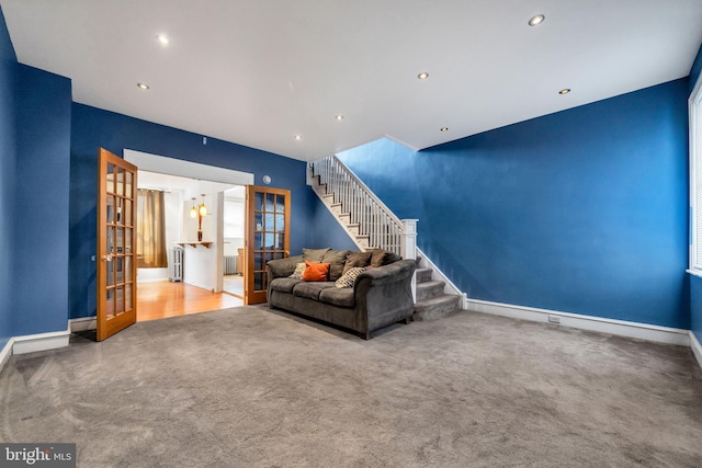 carpeted living room with radiator heating unit, baseboards, stairway, and french doors