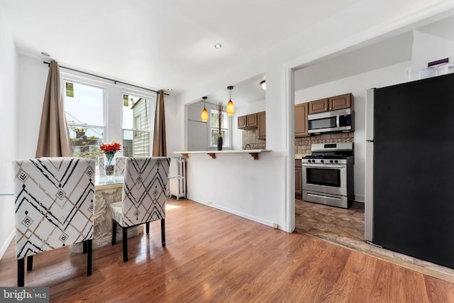 kitchen with a peninsula, a breakfast bar area, light wood-style flooring, appliances with stainless steel finishes, and backsplash