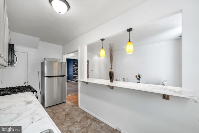 kitchen with freestanding refrigerator, white cabinets, light stone countertops, and a kitchen bar