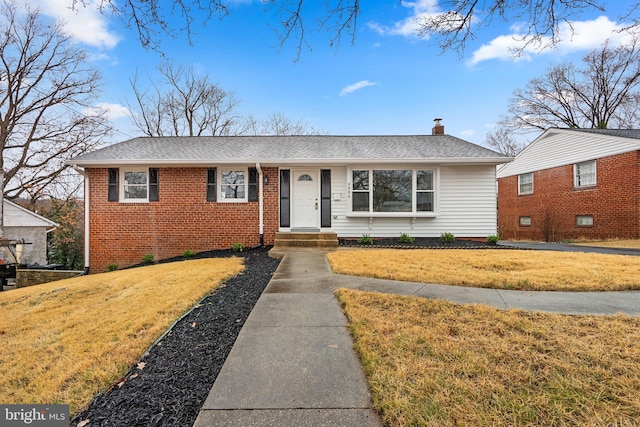 view of front of home featuring brick siding, roof with shingles, a front yard, and a chimney