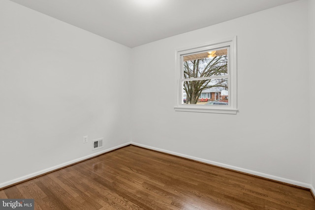 empty room with baseboards, visible vents, and wood finished floors