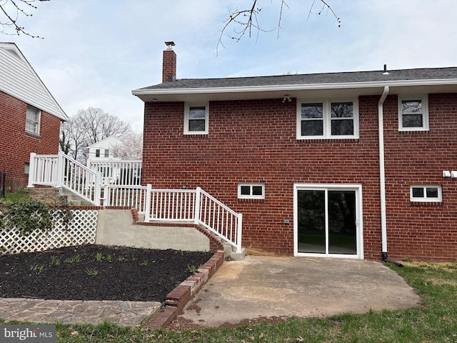 back of property featuring a shingled roof, a chimney, a patio area, and brick siding