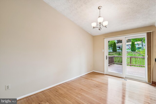 unfurnished room featuring an inviting chandelier, baseboards, light wood finished floors, and a textured ceiling