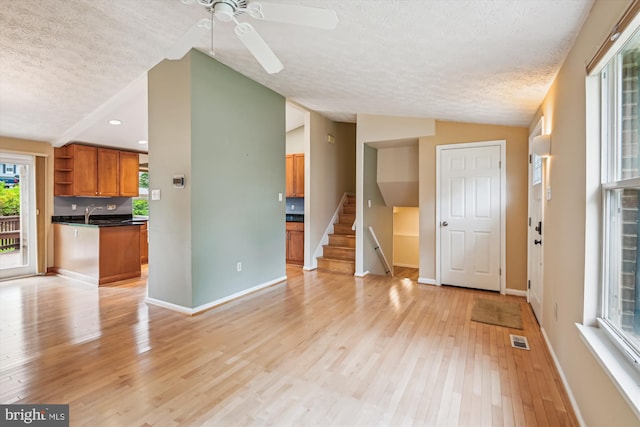 interior space featuring visible vents, baseboards, ceiling fan, light wood-type flooring, and a textured ceiling