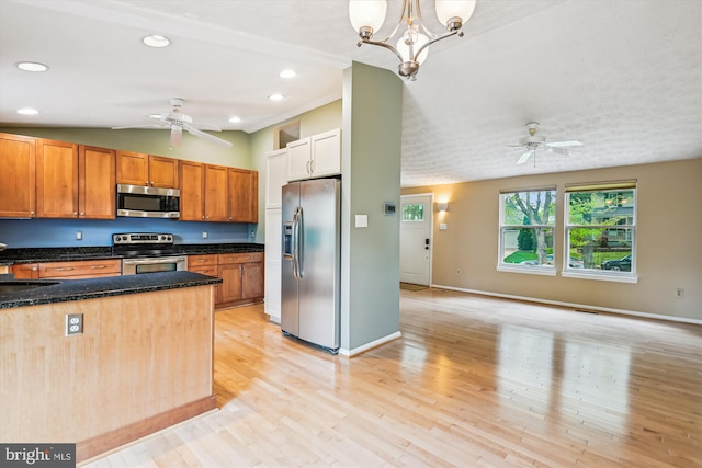 kitchen with appliances with stainless steel finishes, a sink, light wood-style flooring, ceiling fan with notable chandelier, and open floor plan
