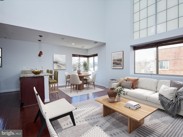 living room featuring baseboards, a towering ceiling, visible vents, and hardwood / wood-style flooring